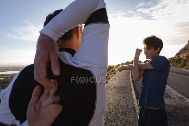 Vista posteriore del padre e del figlio caucasico che fanno esercizio di stretching su strada al mattino — Foto stock