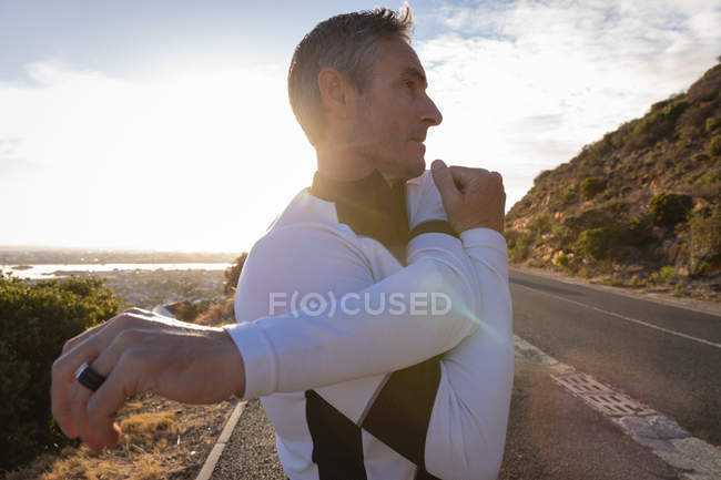 Vista lateral do homem caucasiano maduro fazendo exercício de alongamento na estrada pela manhã — Fotografia de Stock