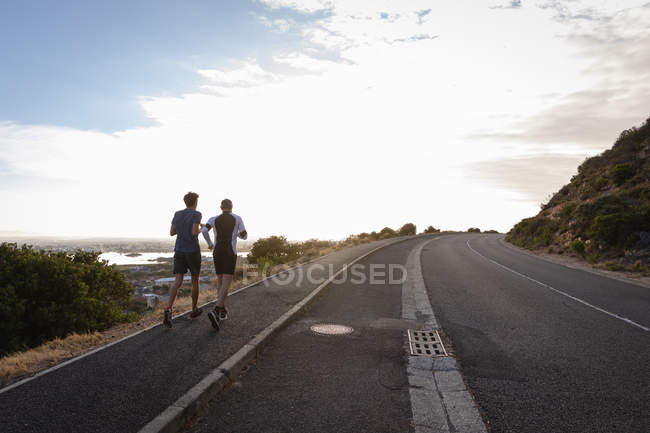 Rear view of father and son jogging on road — Stock Photo