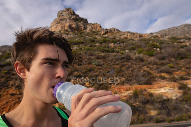 Nahaufnahme eines jungen kaukasischen Mannes, der Wasser auf dem Land trinkt — Stockfoto