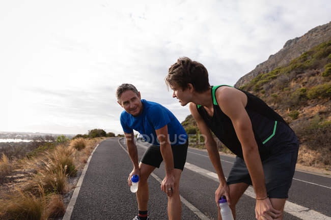 Side view of tired Caucasian father and son with water bottle standing on road — Stock Photo