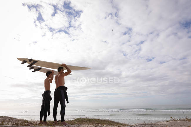 Vista de ángulo bajo del padre y el hijo caucásicos de pie con tabla de surf en la playa - foto de stock
