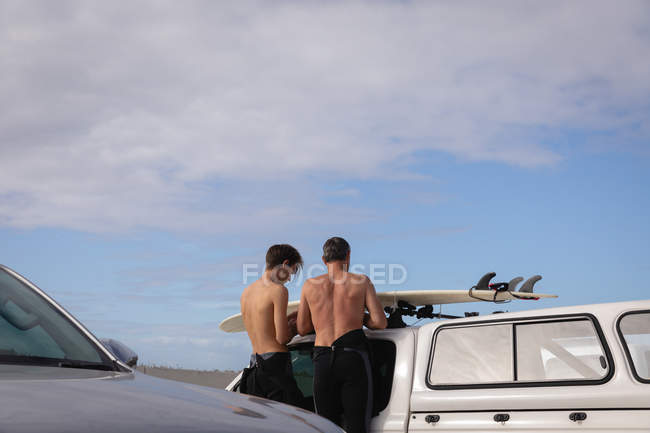 Vista trasera de padre e hijo caucásicos de pie cerca de coche en la playa - foto de stock