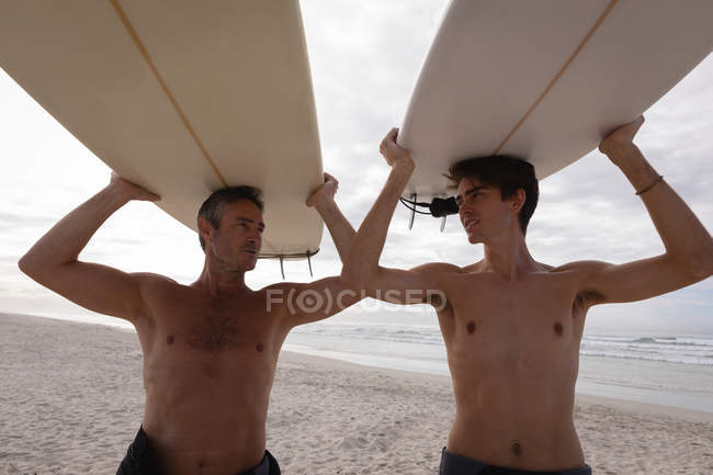 Vista da fonte de pai e filho caucasiano com prancha de surf interagem uns com os outros na praia — Fotografia de Stock
