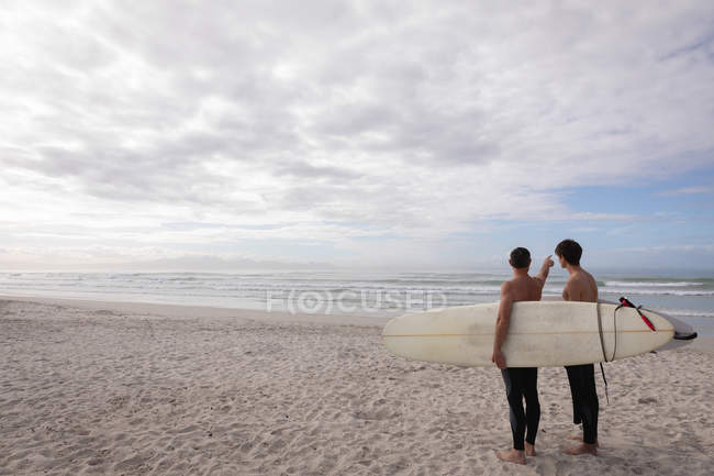 Задний вид на Кавказского отца и сына с доской для серфинга взаимодействуют друг с другом на пляже — стоковое фото