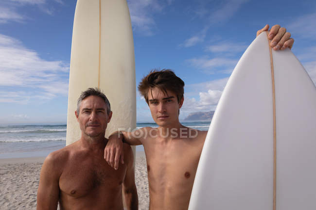 Porträt kaukasischer Vater und Sohn mit Surfbrett am Strand — Stockfoto