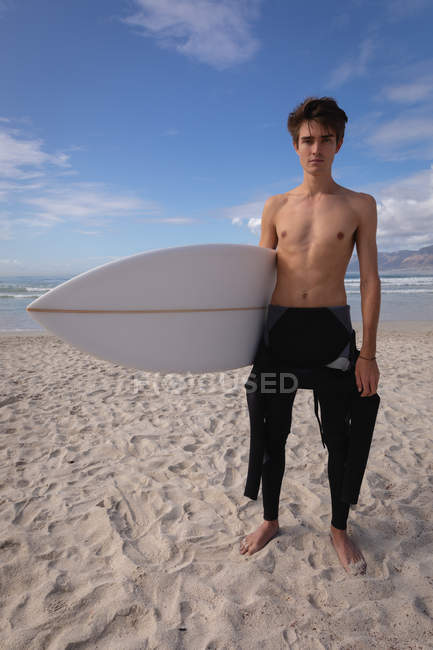 Porträt eines kaukasischen jungen Mannes, der mit Surfbrett am Strand steht — Stockfoto