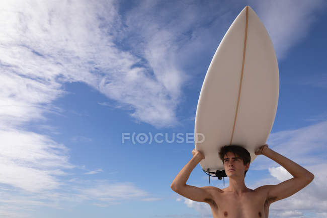 Низкий угол обзора молодого кавказца, стоящего с доской для серфинга на пляже в солнечный день — стоковое фото
