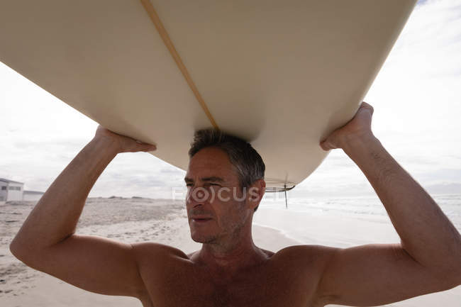 Nahaufnahme eines reifen kaukasischen Mannes, der an einem sonnigen Tag mit einem Surfbrett am Strand steht — Stockfoto