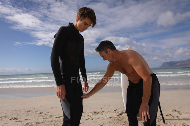 Vista frontal do pai caucasiano ajudando o filho a andar de prancha na praia em um dia ensolarado — Fotografia de Stock