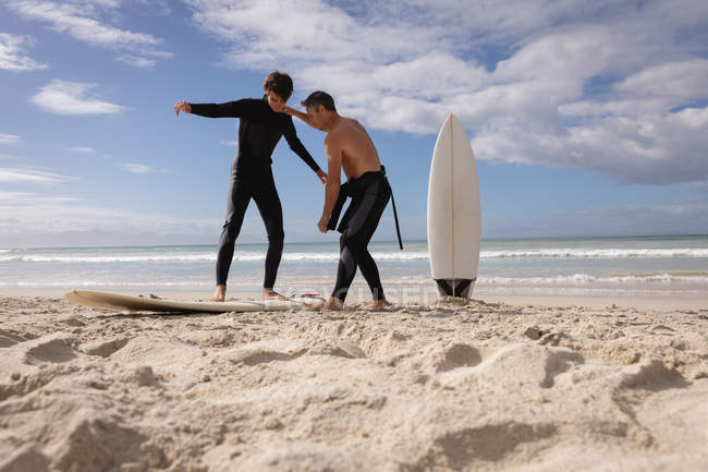 Vue à angle bas du père caucasien aider son fils à monter planche de surf à la plage par une journée ensoleillée — Photo de stock