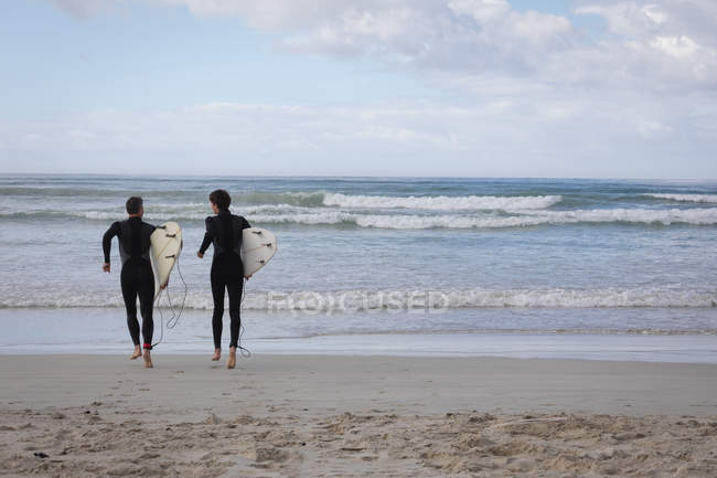 Vista posteriore di padre e figlio caucasico con tavola da surf che corre verso il mare — Foto stock
