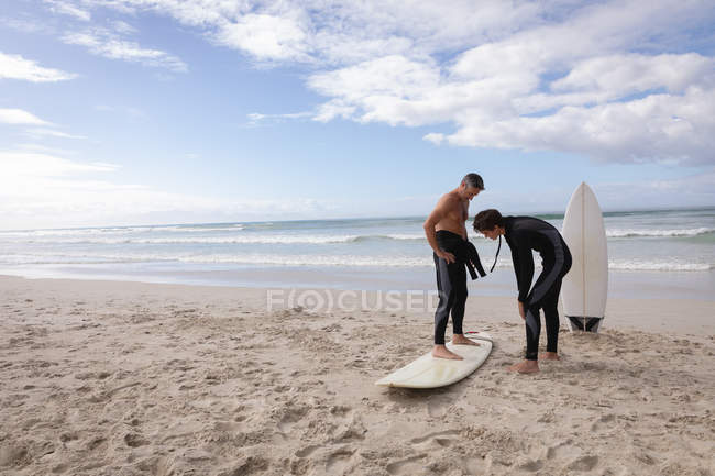 Vista frontal del padre caucásico ayudar a su hijo a montar tabla de surf en la playa en un día soleado - foto de stock