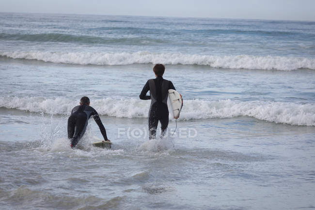Задний вид на Кавказского отца и сына серфинга с доской в море — стоковое фото