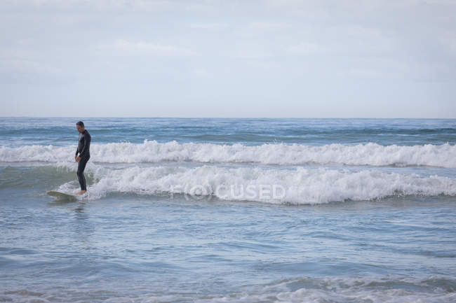 Vorderansicht eines unbeschwerten kaukasischen Mannes mit Surfbrett beim Surfen im Meer — Stockfoto