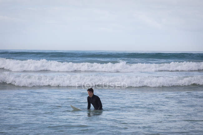 Vista frontal de un joven caucásico despreocupado con tabla de surf surfeando en el mar - foto de stock