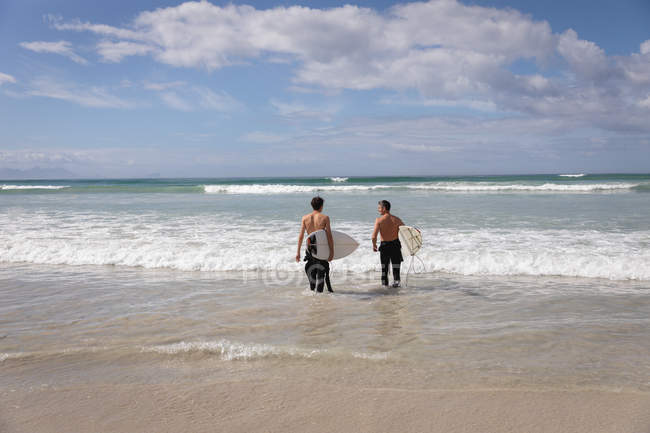 Rückansicht eines kaukasischen Vaters und Sohnes mit Surfbrett im Meer — Stockfoto