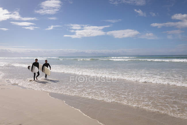 Side view of carefree Caucasian father and son with surfboard walking on beach — Stock Photo