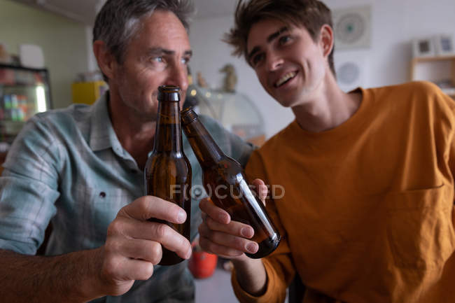 Close-up de pai e filho caucasiano brindando garrafa de cerveja em casa — Fotografia de Stock