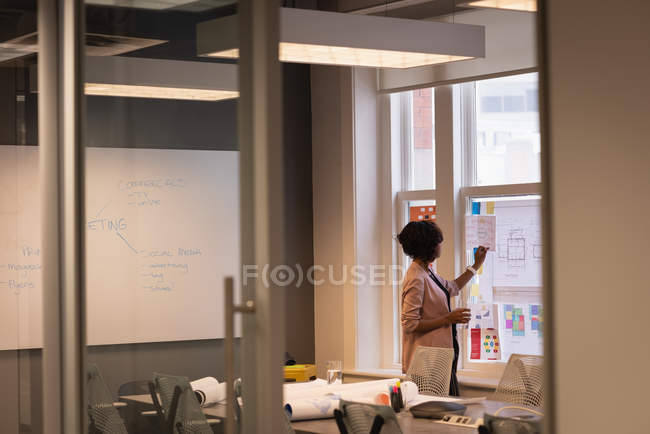 Entfernt von afrikanisch-amerikanischer Geschäftsfrau, die im Konferenzraum im Büro auf ein Diagramm schreibt — Stockfoto