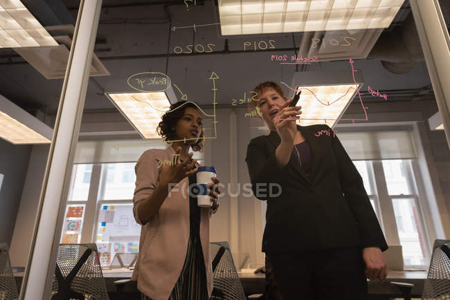 Vista de ángulo bajo de diversas mujeres de negocios que planean en una pared de vidrio en la sala de conferencias en la oficina - foto de stock