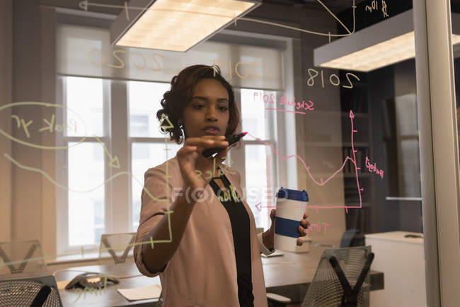 Front view of African American businesswoman writing on glass wall at office — Stock Photo