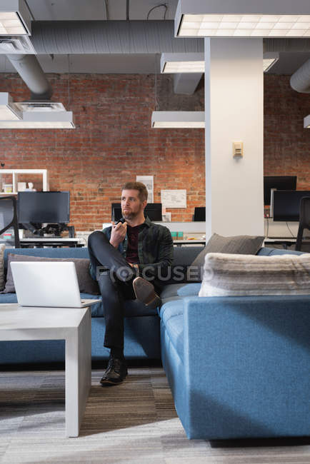 Vista frontal del hombre de negocios reflexivo caucásico sentado en el sofá en la oficina - foto de stock