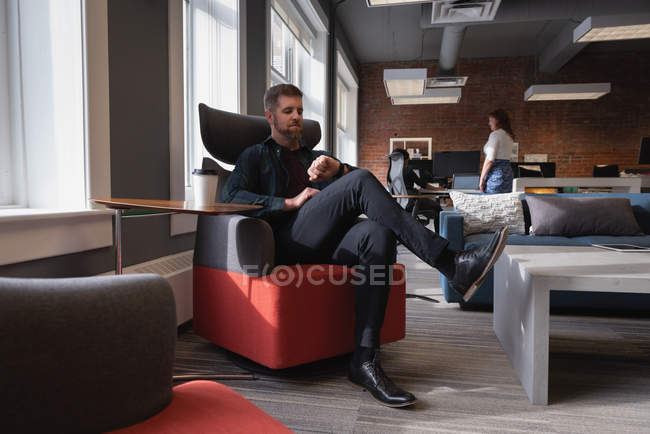 Вид збоку Кавказького бізнесмена дивлячись на його смарт-годинник, сидячи на дивані в офісі — стокове фото