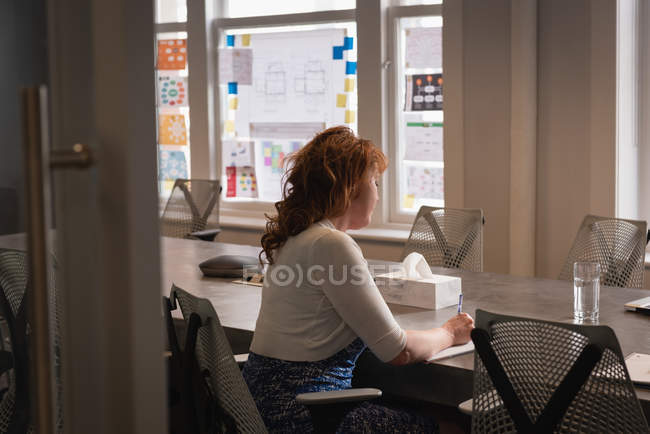 Заднього виду кавказької ділової жінки письмово на щоденник, сидячи за столом в офісі — стокове фото