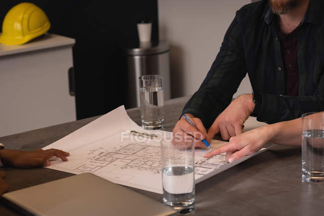 Вид сбоку на архитекторов, работающих на чертежах и бизнес-плане в офисе — стоковое фото
