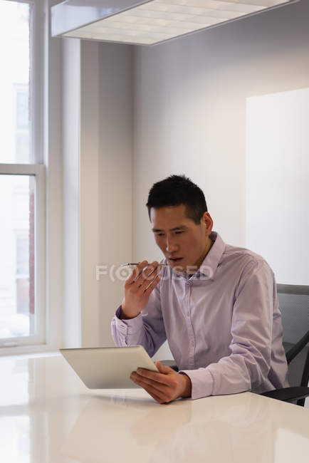 Vista frontal do empresário asiático usando tablet digital enquanto fala no celular no escritório — Fotografia de Stock