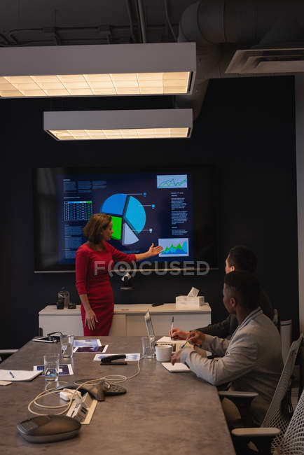 Vista lateral de la diversa mujer de negocios dando presentación a sus colegas en la sala de conferencias - foto de stock