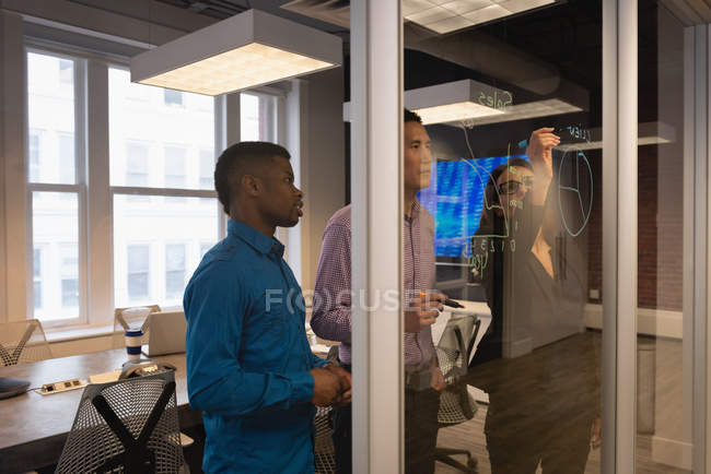 Side view of diverse business people planning on a glass wall in conference room at office — Stock Photo