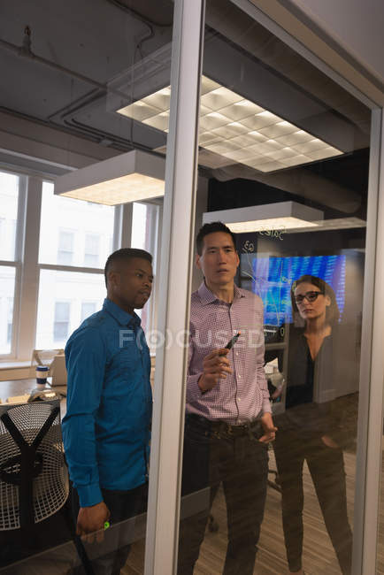 Vista frontal de diversos empresarios que planean en una pared de vidrio en la sala de conferencias en la oficina - foto de stock