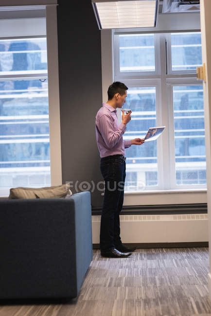 Seitenansicht eines asiatischen Geschäftsmannes, der mit dem Handy telefoniert, während er sich im Büro ein Foto ansieht — Stockfoto