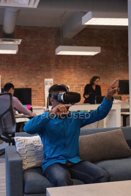 Vista frontal del hombre de negocios afroamericano usando auriculares de realidad virtual en la oficina - foto de stock