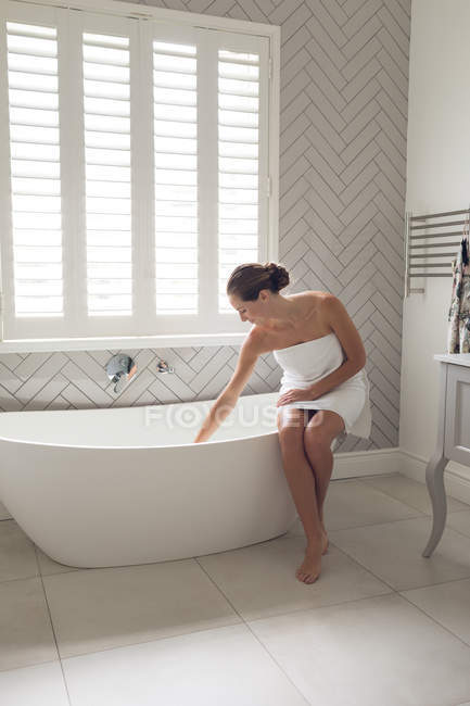 Schöne Frau überprüft den Wasserstand in der Badewanne im Badezimmer — Stockfoto