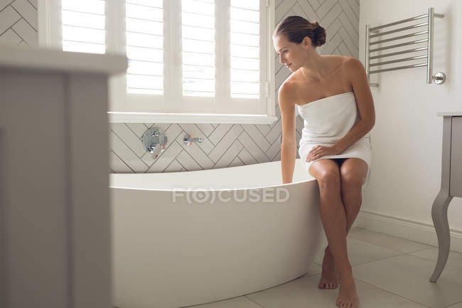 Beautiful woman checking the level of water in the bathtub in bathroom — Stock Photo