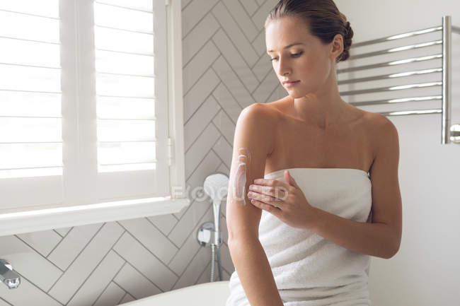 Bella donna che applica lozione sul suo corpo in bagno a casa — Foto stock