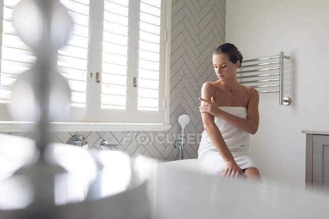 Красива жінка наносить лосьйон на її тіло у ванній вдома — стокове фото