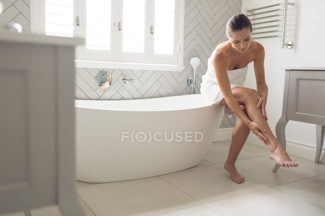 Belle femme appliquant lotion sur son corps dans la salle de bain à la maison — Photo de stock