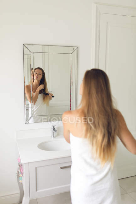 Дзеркальне зображення красивої жінки розчісує волосся у ванній вдома — стокове фото