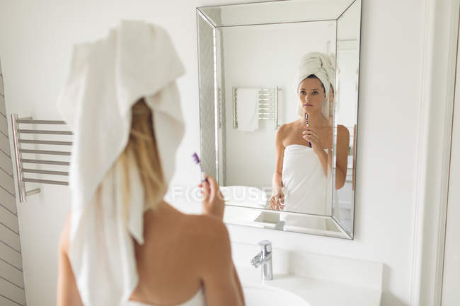 Thoughtful beautiful woman standing in front of mirror while holding toothbrush — Stock Photo