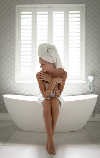 Schöne Frau sitzt am Rand der Badewanne und umarmt sich selbst — Stockfoto