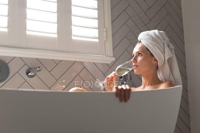 Красивая женщина пьет шампанское в ванной дома — стоковое фото