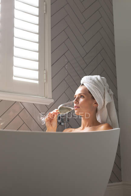 Belle femme ayant du champagne dans la baignoire à la maison — Photo de stock