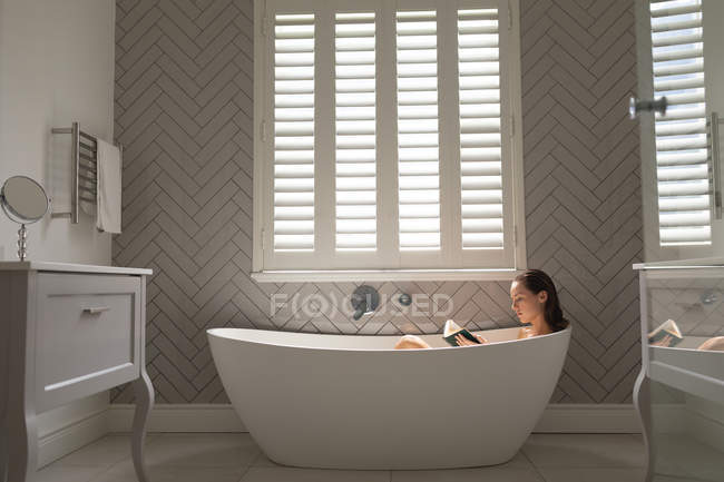 Schöne Frau liest ein Buch in der Badewanne im Badezimmer — Stockfoto