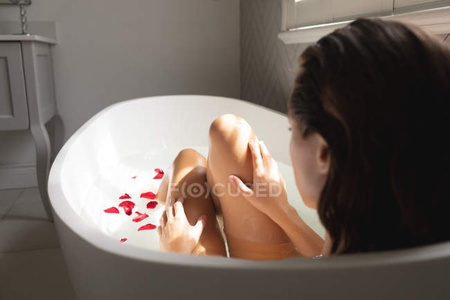 Visão traseira da mulher sentada na banheira com pétalas de rosa — Fotografia de Stock