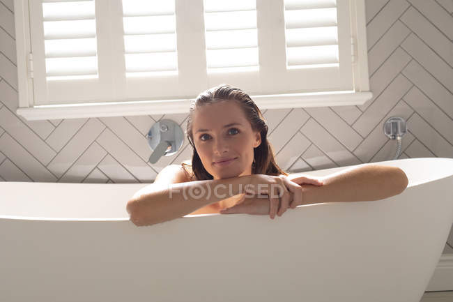 Retrato de mujer sonriente apoyada en la bañera en el baño - foto de stock