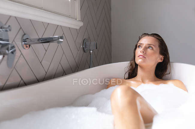Задумчивая женщина купается в ванной комнате дома — стоковое фото